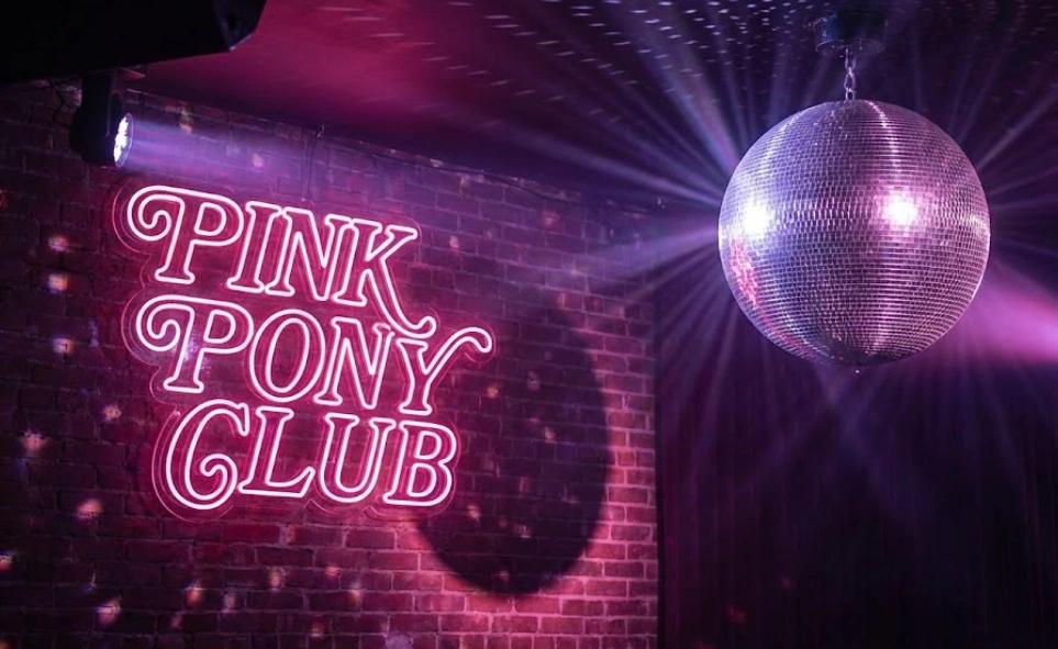 A neon sign for the "PINK PONY CLUB" with a disco ball, capturing the vibrant aesthetic of Chappell Roan's breakout song and her loyal fanbase.